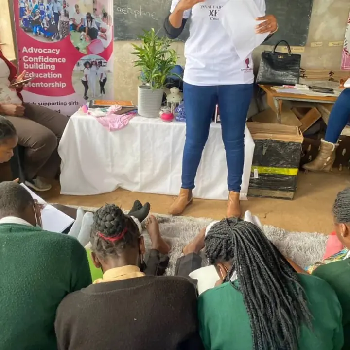 A facilitator speaks while schoolgirls complete activities on the floor.