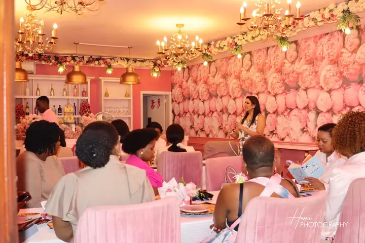 A speaker addresses women in a pink floral venue.